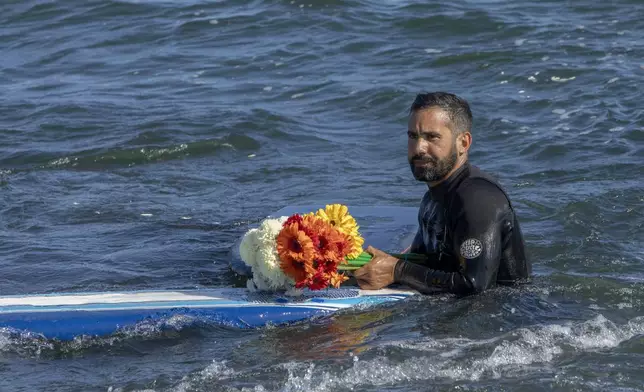 A man holds flowers during a tribute to 3 missing surfers in Ensenada, Mexico, Sunday, May 5, 2024. Mexican authorities said Friday that three bodies were recovered in an area of Baja California near where two Australians and an American went missing last weekend during an apparent camping and surfing trip. (AP Photo/Karen Castaneda)