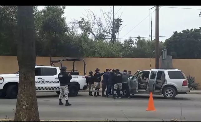 In this image made from video, Mexican security forces frisk men at a checkpoint in Ensenada, Mexico, Thursday, May 2, 2024. Mexican authorities said Thursday they have found tents and questioned a few people in the case of two Australians and an American who went missing over the weekend in the Pacific coast state of Baja California. (AP Photo)
