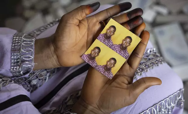 Mariama Sylla, sister of Ousmane Sylla, holds photos of him in their house at Matoto Bonagui, a suburb of Conakry, Guinea, Monday, April 8, 2024. Sylla had landed on Italian shores a year before his death in Feb. 4, 2024, one of tens of thousands of people who pay migrant smugglers hundreds or thousands of euros to cross the Mediterranean to reach Europe. He had no visa, and had been ordered to leave after admitting that he had lied about being a minor. (AP Photo/Misper Apawu)