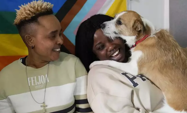 Ella Anthony, left, and her partner Doris Ezuruike Chinons pose for a photo with their dog Paddy, during an interview in their house in Passo Corese, near Rome, Monday, March 11, 2024. Knowing that she faced a possible prison term since Nigeria criminalizes same-sex relationships, Anthony fled with her partner to Libya in 2014 and then Italy, where they both won asylum. Their claim? That they had a well-founded fear of anti-LGBTQ+ persecution back home. (AP Photo/Alessandra Tarantino)