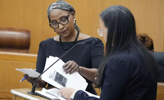 Lisa Ross, attorney for Bul Mabil, brother of Dau Mabil, a 33-year-old Jackson, Miss., resident who went missing on March 25 and whose body was found in April floating in the Pearl River in Lawrence County, left, gives Paloma Wu, attorney for Karissa Bowley, wife of the deceased, a set of her client's texts during a hearing on whether a judge should dissolve or modify his injunction preventing the release of Mabil's remains until an independent autopsy could be conducted, Tuesday, April 30, 2024, in Jackson, Miss. (AP Photo/Rogelio V. Solis)