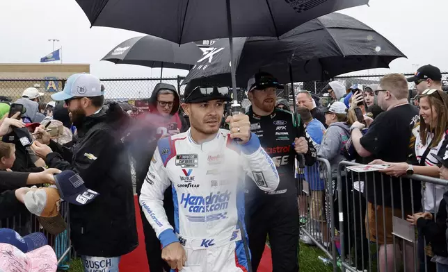 NASCAR Cup Series points leader Kyle Larson, center, walks to a track meeting as rain falls before a NASCAR Cup Series auto race at Kansas Speedway in Kansas City, Kan., Sunday, May 5, 2024. (AP Photo/Colin E. Braley)