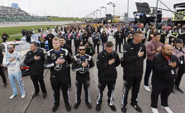 Ross Chastain, left, along with other drivers and crews stand along pit road during the playing of the National Anthem before a NASCAR Cup Series auto race at Kansas Speedway in Kansas City, Kan., Sunday, May 5, 2024. (AP Photo/Colin E. Braley)
