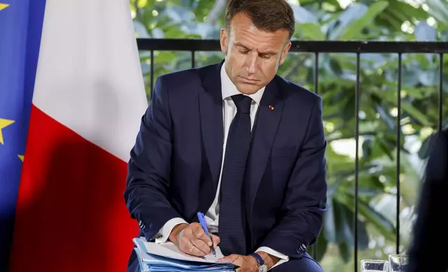 French President Emmanuel Macron takes notes during a meeting with New Caledonia's elected officials and local representatives at the French High Commissioner Louis Le Franc's residence in Noumea, New Caledonia, Thursday, May 23, 2024. Macron has landed in riot-hit New Caledonia, having crossed the globe by plane from Paris in a high-profile show of support for the French Pacific archipelago wracked by deadly unrest and where indigenous people have long sought independence from France. (Ludovic Marin/Pool Photo via AP)