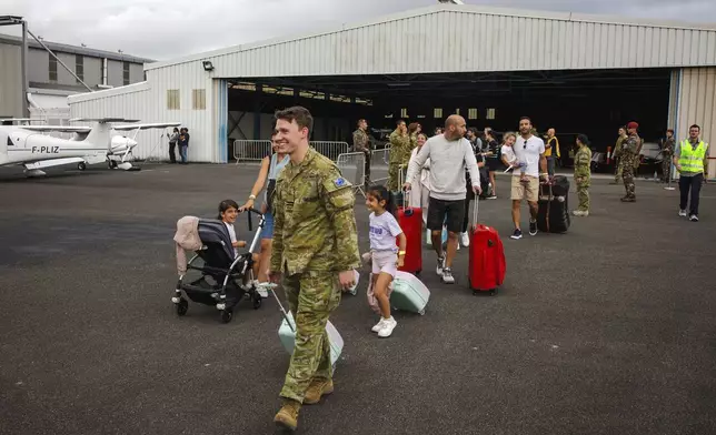 In this photo provided by the Australian Defence Force, Royal Australian Air Force Officer, Flight Lieutenant Thomas Rogers, second left, assists Australian and other tourists to a waiting plane for departure from Noumea, New Caledonia, Tuesday, May 21, 2024. The Australian military had flown 115 passengers in two flights from the restive French Pacific territory of New Caledonia and would continue to work with France to repatriate all Australians who want to leave, an Australian government minister said Wednesday, May 22, 2024. (LAC Adam Abela/ADF via AP)