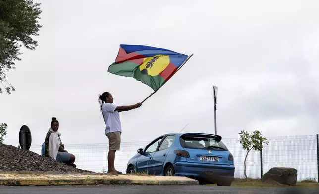 A woman waves a Kanak and Socialist National Liberation Front (FLNKS) flag in Noumea, New Caledonia, Wednesday May 15, 2024. France has imposed a state of emergency in the French Pacific territory of New Caledonia. The measures imposed on Wednesday for at least 12 days boost security forces' powers to quell deadly unrest that has left four people dead, erupting after protests over voting reforms. (AP Photo/Nicolas Job)