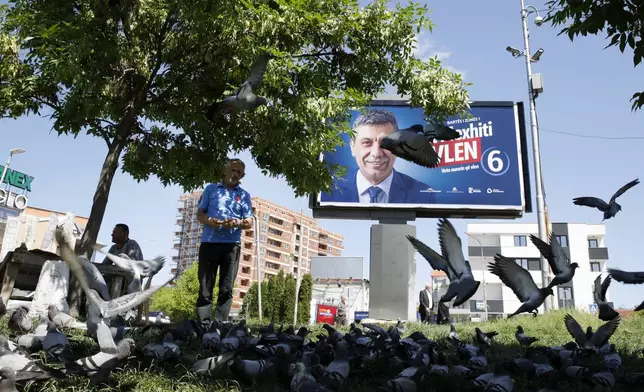 A man feeds pigeons near an electoral poster of Izet Mexhiti from the ethnic Albanian opposition party VLEN, in a street in Skopje, North Macedonia, on Monday, May 6, 2024. Voters go to the polls on Wednesday in North Macedonia to cast ballots for parliamentary election and presidential runoff, for the second time in two weeks. (AP Photo/Boris Grdanoski)