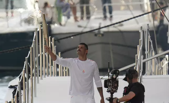 First torch carrier in France French Olympic swimmer Florent Manaudou holds the Olympic torch after leaving The Belem, the three-masted sailing ship in the Old port of Marseille, southern France, Wednesday, May 8, 2024. After leaving Marseille, a vast relay route is undertaken before the torch odyssey ends on July 27 in Paris. The Paris 2024 Olympic Games will run from July 26 to Aug.11, 2024. (AP Photo/Thibault Camus)