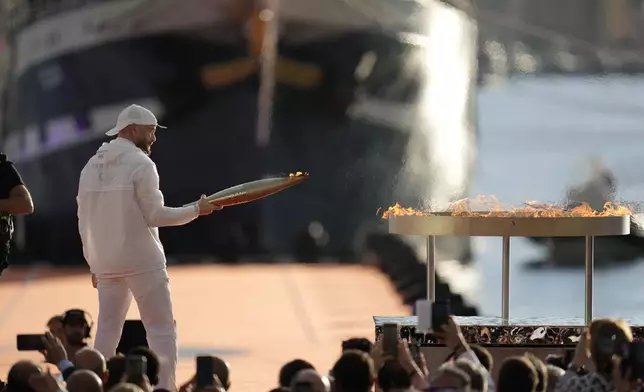 French rap artist Jul lights the Olympic cauldron with the Olympic torch during the torch arrival ceremony in Marseille, southern France, Wednesday May 8, 2024. After leaving Marseille, a vast relay route is undertaken before the torch odyssey ends on July 27 in Paris. The Paris 2024 Olympic Games will run from July 26 to Aug.11, 2024. (AP Photo/Thibault Camus)