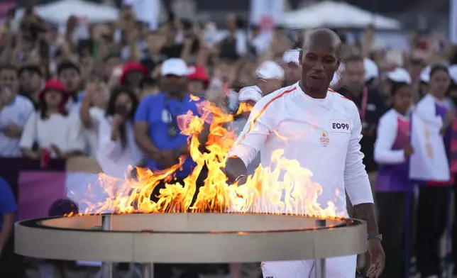 Torchbearer Didier Drogba of France holds the Olympic torch to light the cauldron at the Velodrome stadium in Marseille, southern France, Thursday, May 9, 2024. Torchbearers are to carry the Olympic flame through the streets of France's southern port city of Marseille, one day after it arrived on a majestic three-mast ship for the welcoming ceremony. (AP Photo/Daniel Cole)