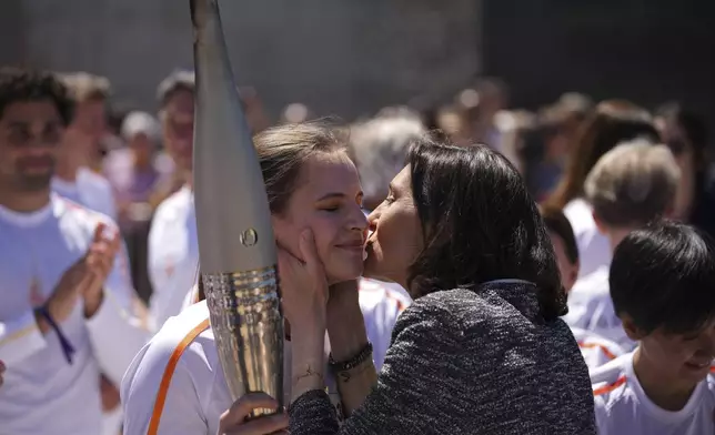 French Sports Minister Amelie Oudea-Castera, right, kisses Maria Vysotchanska of Ukraine on the cheek during the Olympic torch relay in Marseille, southern France, Thursday, May 9, 2024. Torchbearers are to carry the Olympic flame through the streets of France' s southern port city of Marseille, one day after it arrived on a majestic three-mast ship for the welcoming ceremony. (AP Photo/Daniel Cole)