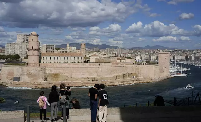 People stand in the gardens overlooking the Old Port, in Marseille, southern France, Tuesday, May 7, 2024. The Olympic torch will finally enter France when it reaches the southern seaport of Marseille on Wednesday. (AP Photo/Thibault Camus)