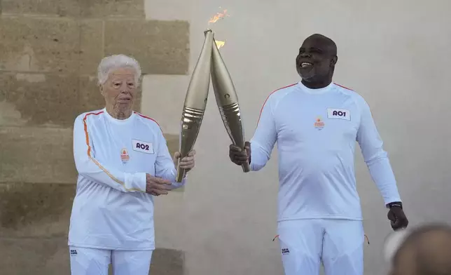 French torchbearers Colette Cataldo, left, and Basile Boli perform a torch kiss during the first stage of the Olympic torch relay in Marseille, southern France, Thursday, May 9, 2024. Torchbearers are to carry the Olympic flame through the streets of France' s southern port city of Marseille, one day after it arrived on a majestic three-mast ship for the welcoming ceremony. (AP Photo/Thibault Camus)