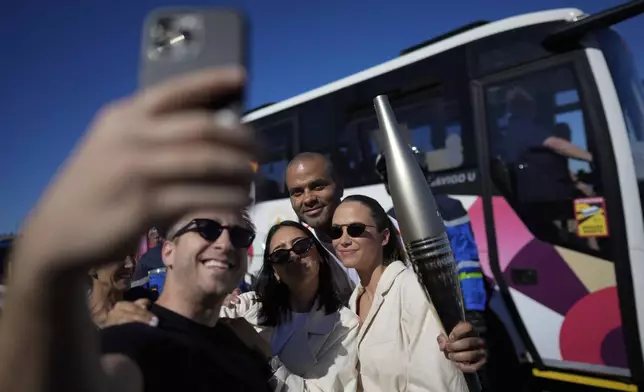 French torchbearer Tony Parker, rear center, poses for a selfie as he participates in the first stage of the Olympic torch relay in Marseille, southern France, Thursday, May 9, 2024. Torchbearers are to carry the Olympic flame through the streets of France' s southern port city of Marseille, one day after it arrived on a majestic three-mast ship for the welcoming ceremony. (AP Photo/Thibault Camus)