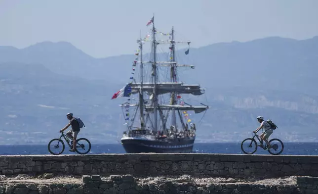 FILE - Cyclists pass in front of the Belem, the three-masted sailing ship carrying the Olympic flame to France, as it sails near Corinth, Greece, April 28, 2024. The Olympic torch finally enters France when it reaches the southern seaport of Marseille on Wednesday May 8, 2024, on an armada from Greece. After leaving Marseille a vast relay route will be undertaken before the torch's odyssey ends on July 27 in Paris. (AP Photo/Petros Giannakouris, File)