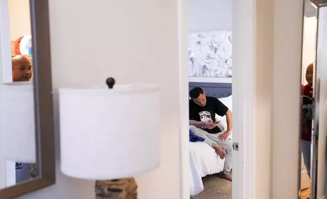 Richard Zambales is reflected in a mirror doing laundry while Reyner Dagalea, center, looks down at his phone at a temporary rental house in Lacey, Wash., on Tuesday, Jan. 30, 2024. They are part of a group of six men at the house who were among two dozen Filipino crew members confined to tuna fishing vessels for months last year without U.S. visas in Westport, Wash. while waiting for backpay from their employer, McAdam's Fish, and recruitment agency Pescadores International. (AP Photo/Lindsey Wasson)