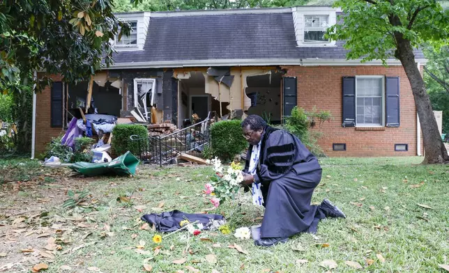 Rev. Raymond Johnson, of Marion, S.C., arranges flowers on the lawn of the home on Galway Drive in Charlotte, N.C., Tuesday, April 30, 2024 where a shootout between a suspect and officers occurred during an attempt to serve a warrant on April 29, 2024. (AP Photo/Nell Redmond)