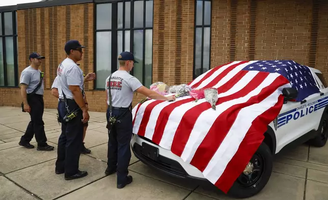 Charlotte firefighters from Engine 7 bring flowers to a flag-covered Charlotte-Mecklenburg police vehicle at the North Tryon Station in Charlotte, N.C., Tuesday, April 30, 2024, where Charlotte-Mecklenburg Officer Joshua Eyer was stationed. Police in North Carolina say a shootout that killed several law enforcement officers, including Eyer, and wounded others began as officers approached a home on Monday to serve a warrant for a felon wanted for possessing a firearm. (AP Photo/Nell Redmond)