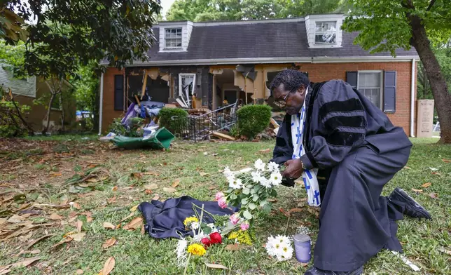 Rev. Raymond Johnson, of Marion, S.C., arranges flowers on the lawn of the home on Galway Drive in Charlotte, N.C., Tuesday, April 30, 2024 where a shootout between a suspect and officers occurred during an attempt to serve a warrant on Monday. Four law enforcement officers were killed. (AP Photo/Nell Redmond)