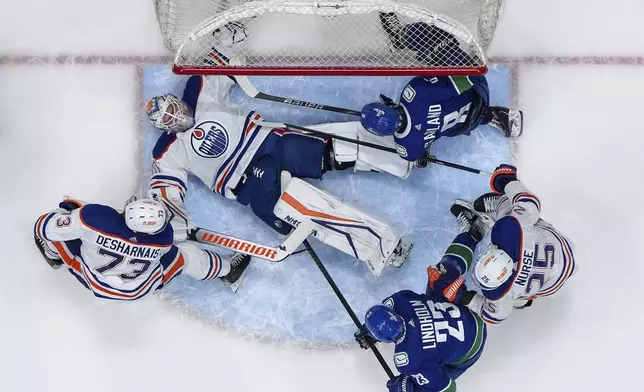 Edmonton Oilers goalie Calvin Pickard, centre, lies on the ice with the puck under him after making a save as Vincent Desharnais (73), Darnell Nurse (25) and Vancouver's Conor Garland (8) and Elias Lindholm (23) watch during the first period in Game 5 of an NHL hockey Stanley Cup second-round playoff series, in Vancouver, on Thursday, May 16, 2024. (Darryl Dyck/The Canadian Press via AP)