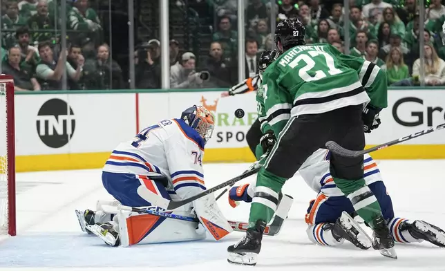 Edmonton Oilers goaltender Stuart Skinner (74) defends against an airborne puck under pressure from Dallas Stars left wing Mason Marchment (27) during the first period of Game 1 of the Western Conference finals in the NHL hockey Stanley Cup playoffs Thursday, May 23, 2024, in Dallas. (AP Photo/Tony Gutierrez)