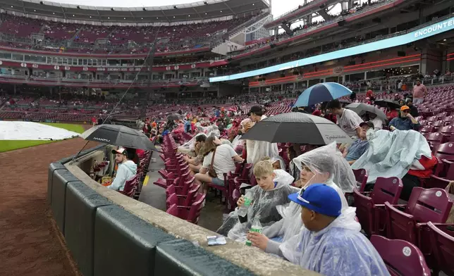 Fans wait in the rain during a rain delay before a baseball game between the Baltimore Orioles and the Cincinnati Reds, Friday, May 3, 2024, in Cincinnati. (AP Photo/Carolyn Kaster)