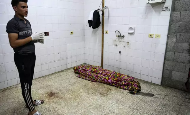 A Palestinian medic stands near a body while he waits for other bodies killed in the Israeli bombardment of the Gaza Strip at the morgue of Al Aqsa hospital in Deir al Balah, central Gaza Strip, on Sunday, May 26, 2024. (AP Photo/Abdel Kareem Hana)