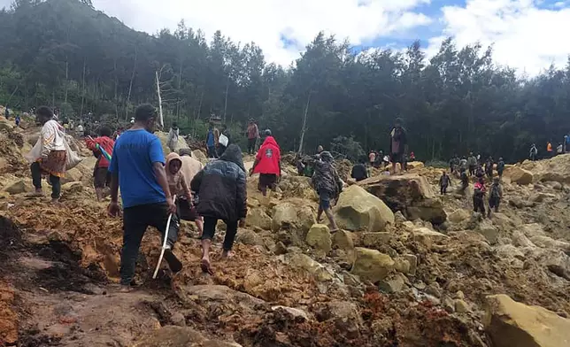 In this photo provided by the International Organization for Migration, people cross over the landslide area to get to the other side in Yambali village, Papua New Guinea, Friday, May 24, 2024. More than 100 people are believed to have been killed in the landslide that buried a village and an emergency response is underway, officials in the South Pacific island nation said. The landslide struck Enga province, about 600 kilometers (370 miles) northwest of the capital, Port Moresby, at roughly 3 a.m., Australian Broadcasting Corp. reported. (Benjamin Sipa/International Organization for Migration via AP)