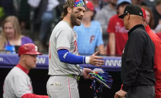 Philadelphia Phillies' Bryce Harper argues with second base umpire Vic Carpazza, right, as manager Rob Thomson, back right, listens after Harper was ejected for arguing after striking out to end the top of the first inning of the team's baseball game against the Colorado Rockies on Friday, May 24, 2024, in Denver. (AP Photo/David Zalubowski)