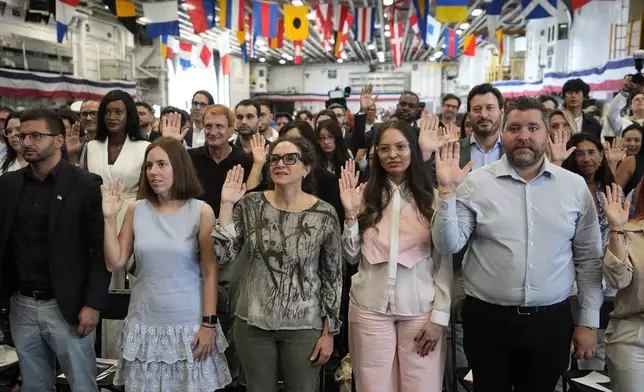 People raise their right hand as they take the Oath of Allegiance to the United States of America during a naturalization ceremony aboard the USS Bataan during Fleet Week Miami at PortMiami, Tuesday, May 7, 2024, in Miami. (AP Photo/Lynne Sladky)