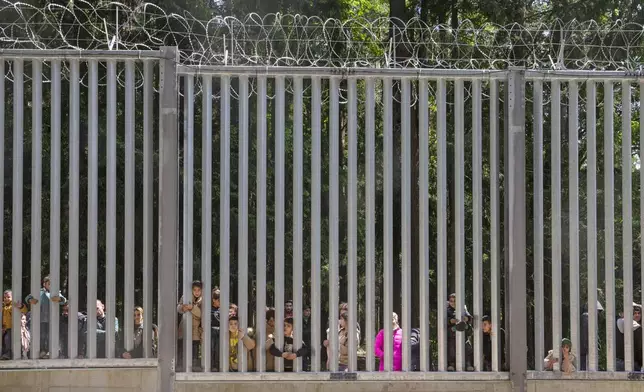 FILE - Members of a group of some 30 migrants seeking asylum look through the railings of a wall that Poland has built on its border with Belarus to stop massive migrant pressure, in Bialowieza, Poland, on May 28, 2023. Defense officials in NATO member Poland were presenting plans Monday, May 27, 2024, for fortifications and strengthening of its eastern border with Russia and Moscow ally Belarus. (AP Photo/Agnieszka Sadowska, File)