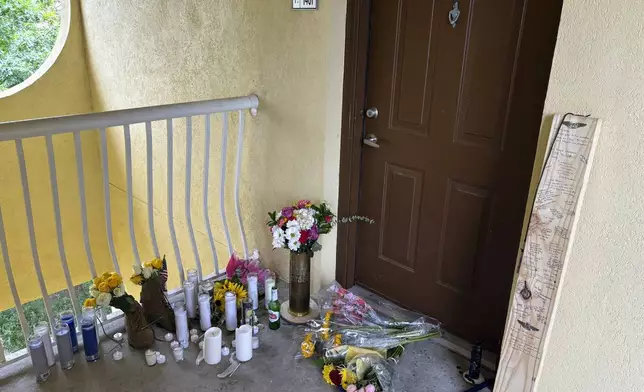 A small shrine is pictured Monday, May 13, 2024, in Fort Walton Beach, Fla. at the door of an apartment where a Florida deputy shot and killed Senior Airman Roger Fortson. The shrine includes a long wooden plank, anchored by two sets of aviator wings and a black marker to leave thoughts, a Stella Artois, and combat boots and an American Flag. As the unit takes a day to grieve and prepare for a funeral Friday, May 17, questions remain about the shooting. (AP Photo)