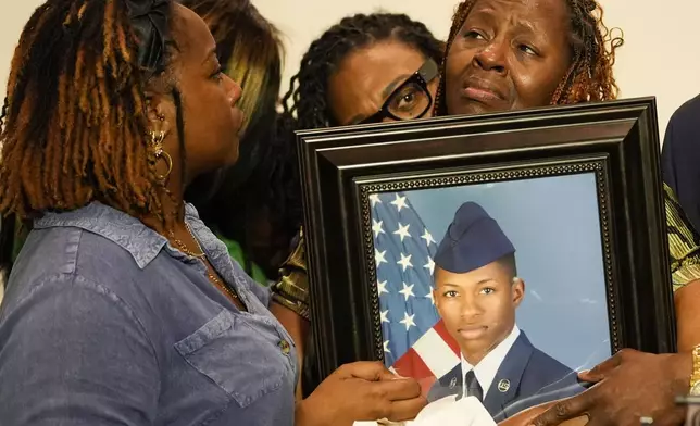 Chantimekki Fortson, mother of Roger Fortson, a U.S. Navy airman, is comforted by family as she holds a photo of her son during a news conference regarding his death, along with family and Attorney Ben Crump, in Ft. Walton Beach, Fla. Fortson was shot and killed by police in his apartment on May 3, 2024. (AP Photo/Gerald Herbert)