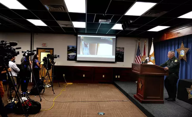 Okaloosa County Sheriff Eric Aden holds a news conference where he shared deputy body cam footage, displayed on screen at center, of the May 3, 2024 shooting of Roger Fortson, a U.S. Navy airman, Thursday, May 9, 2024, in Fort Walton Beach, Fla. Fortson was shot in his apartment after a response to a complaint. (AP Photo/Gerald Herbert)