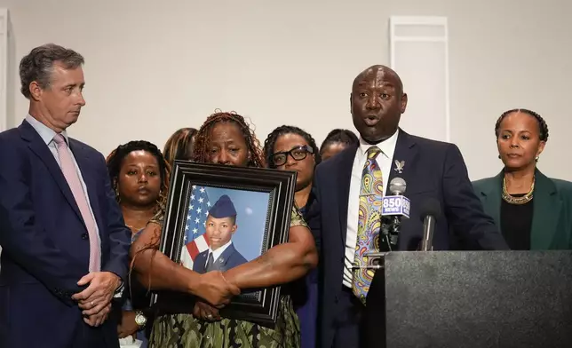 Chantimekki Fortson, mother of Roger Fortson, a U.S. Navy airman, holds a photo of her son during a news conference regarding his death, along with family and Attorney Ben Crump, right, and Brian Bar, left, Thursday, May 9, 2024, in Ft. Walton Beach, Fla. Fortson was shot and killed by police in his apartment on May 3, 2024. Far right is attorney Natalie Jackson. (AP Photo/Gerald Herbert)
