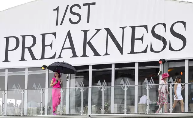 A woman takes shelter from light rain under an umbrella ahead of the Preakness Stakes horse race at Pimlico Race Course, Saturday, May 18, 2024, in Baltimore. (AP Photo/Nick Wass)