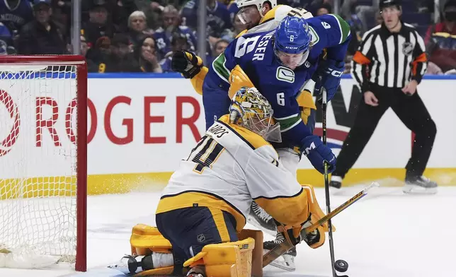 Nashville Predators goalie Juuse Saros, bottom, stops Vancouver Canucks' Brock Boeser, middle, as he is checked by Nashville Predators' Alexandre Carrier during the third period in Game 5 of an NHL hockey Stanley Cup first-round playoff series, in Vancouver, British Columbia, on Tuesday, April 30, 2024. (Darryl Dyck/The Canadian Press via AP)