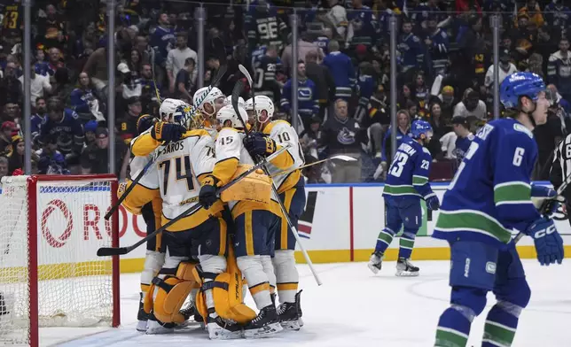 Nashville Predators players celebrate with goalie Juuse Saros (74) as Vancouver Canucks' Elias Lindholm (23) and Brock Boeser (6) skate off the ice after Nashville defeated Vancouver in Game 5 of an NHL hockey Stanley Cup first-round playoff series, in Vancouver, British Columbia, on Tuesday, April 30, 2024. (Darryl Dyck/The Canadian Press via AP)