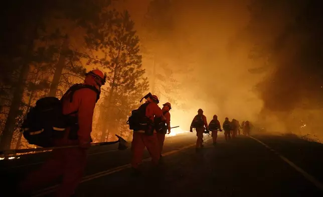 FILE - Inmate firefighters walk along Highway 120 after a burnout operation during the Rim Fire near Yosemite National Park, Calif., on Sunday, Aug. 25, 2013. California currently has about 1,250 prisoners trained to fight fires and has used them since the 1940s. It pays its "Angels in Orange" $2.90 to $5.12 a day, plus an extra $1 an hour when they work during emergencies. (AP Photo/Jae C. Hong, File)