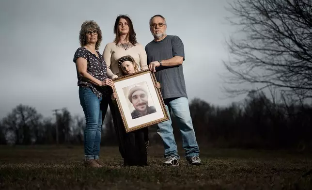 Eight-year-old Estella Snyder, accompanied by her mother, Ashley Snyder, and grandparents Jackie and Brian Baraniak pose for a photograph with an image of her deceased father, Matthew Baraniak, in Halifax, Pa., Wednesday, March 6, 2024. Across the country, it's not uncommon for the relatives of prisoners who died on the job to struggle with determining who's liable. When workers' compensation is offered, the amount awarded is typically determined by the size of the worker's paycheck and usually closes the door on future wrongful death suits. (AP Photo/Matt Rourke)