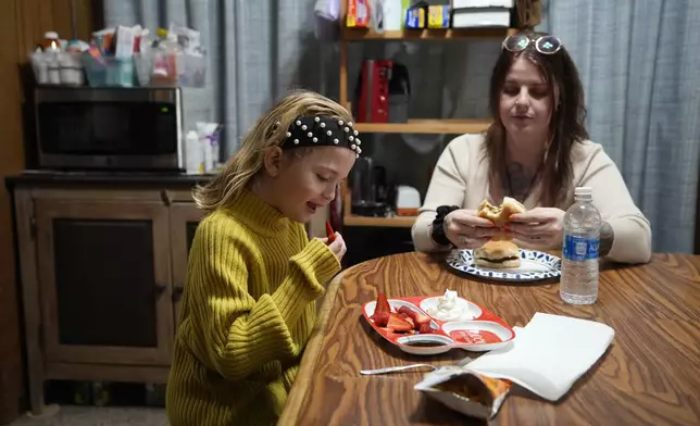 Eight-year-old Estella Snyder has a snack with her mother Ashley Snyder in Halifax, Pa., Wednesday, March 6, 2024. Across the country, it's not uncommon for the relatives of prisoners who died on the job to struggle with determining who's liable. When workers' compensation is offered, the amount awarded is typically determined by the size of the worker's paycheck and usually closes the door on future wrongful death suits. (AP Photo/Matt Rourke)