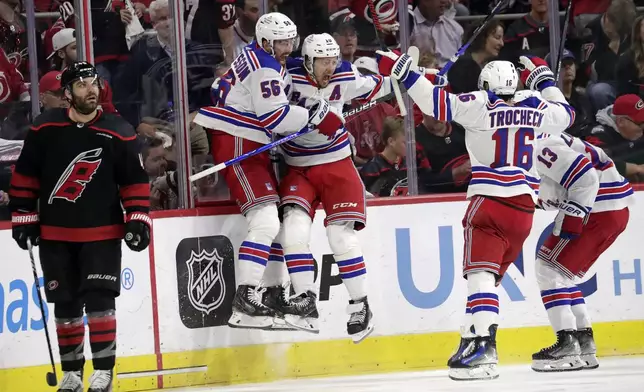 New York Rangers defenseman Erik Gustafsson (56), left wing Artemi Panarin, center Vincent Trocheck (16) and left wing Alexis Lafrenière (13) celebrate after scoring the winning goal in the overtime period in Game 3 of an NHL hockey Stanley Cup second-round playoff series Thursday, May 9, 2024, in Raleigh, N.C. Carolina Hurricanes left wing Jordan Martinook skates away at left. (AP Photo/Chris Seward)
