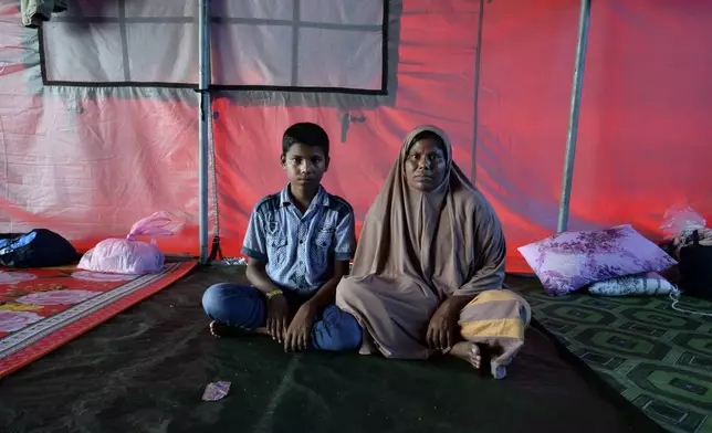 Rohingya refugee Rahena Begum, right, and her 13-year-old son, Noor Shahed, pose for a photograph at a temporary shelter in Meulaboh, Indonesia, on Thursday, April 4, 2024. They were among 75 people rescued in March from atop the overturned hull of a boat that capsized off Indonesia's coast. Dozens of others, including Rahena's 9-year-old daughter and 12-year-old son, died. (AP Photo/Reza Saifullah)