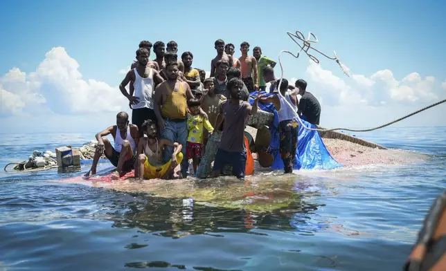 Ethnic Rohingya refugees stand on their capsized boat as rescuers throw a rope to them off West Aceh, Indonesia, on Thursday, March 21, 2024. The wooden fishing boat carried about 140 Rohingya refugees, but only 75 people were rescued. In interviews with The Associated Press, eight of the survivors described abuses on board. (AP Photo/Reza Saifullah)