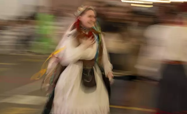 A woman wearing a traditional Ukrainian costume dances with others at a market in Kyiv, Ukraine, Sunday, April 28, 2024. (AP Photo/Francisco Seco)