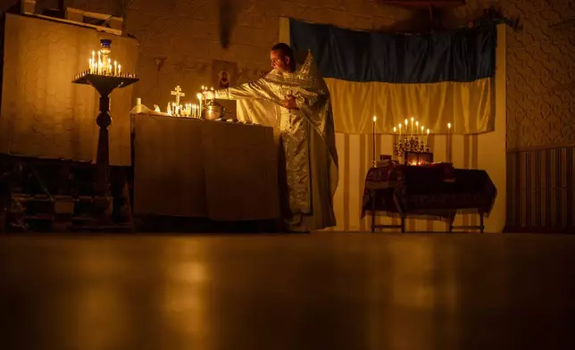 Priest Ivan, chaplain of the 72nd Separate Mechanized Brigade of the Ukrainian army, lights candles during a Christian Orthodox Easter religious service, in Donetsk region, Ukraine, Saturday, May 4, 2024. (AP Photo/Francisco Seco)