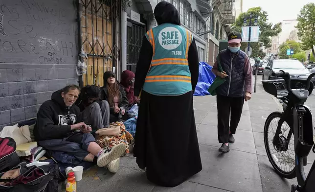 Tatiana Alabsi, center, talks to a group of people sitting on a sidewalk in the Tenderloin neighborhood Wednesday, April 24, 2024, in San Francisco. (AP Photo/Godofredo A. Vásquez)