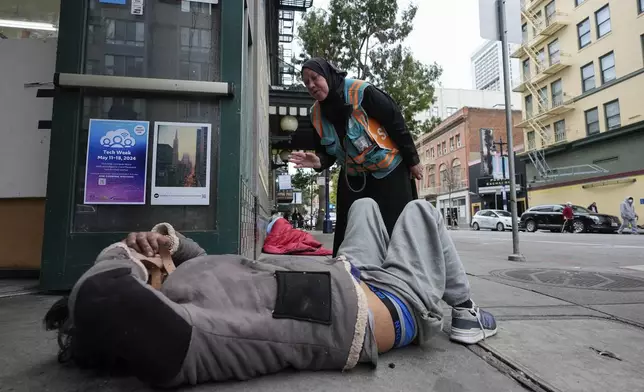 Tatiana Alabsi, right, checks on a man laying on a sidewalk and asks him to please move before children start walking to school in the Tenderloin neighborhood Wednesday, April 24, 2024, in San Francisco. (AP Photo/Godofredo A. Vásquez)