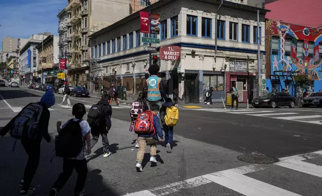 Children are escorted safely across an intersection in the Tenderloin neighborhood Wednesday, March 20, 2024, in San Francisco. (AP Photo/Godofredo A. Vásquez)