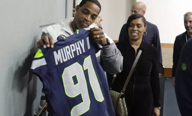 The parents of Seattle Seahawks 2024 first-round NFL football draft pick Byron Murphy II, Bryon Murphy Sr., left, and mother Seneca Murphy, second from left, look at their son's jersey after a news conference at the team's headquarters Thursday, May 2, 2024, in Renton, Wash. (AP Photo/John Froschauer)